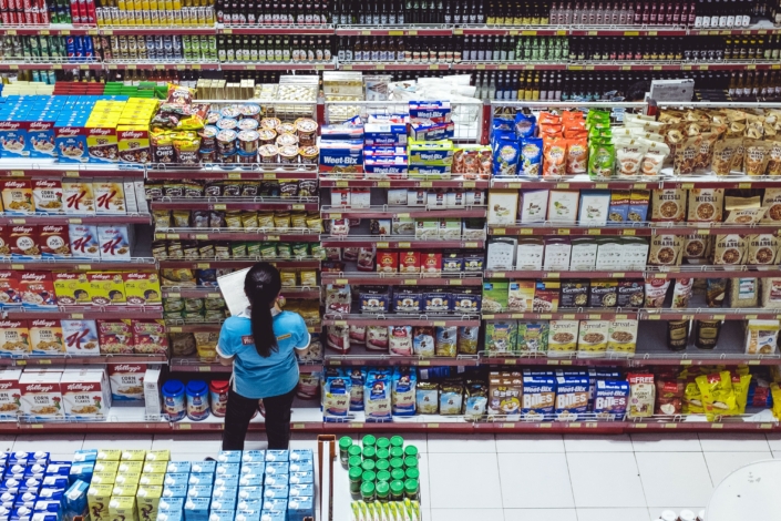 Mitarbeiterin eines Supermarkts steht vor den Regalen und kontrolliert die Waren, Foto Bernard Hermant auf Unsplash
